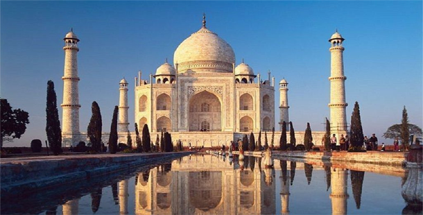 A large white building with domes and a pool of water with taj mahal in the background