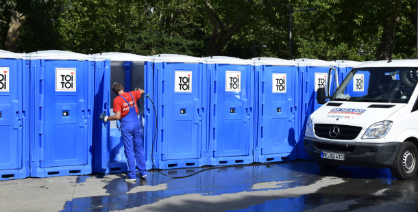 A person in a blue uniform standing next to a row of portable toilets