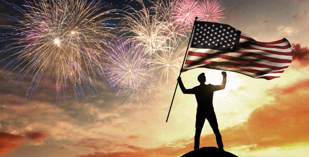 A person holding a flag and fireworks in the sky