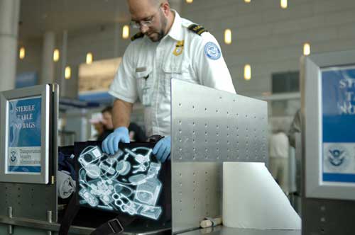 TSA agent inspecting bag with Xray items on outside