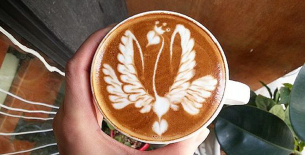 A latte with an intricate drawing of a swam with the shape of a heart as a head.