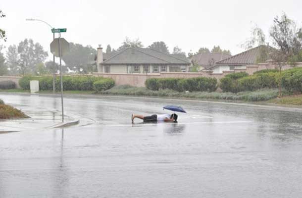 planking in the middle of the street, in the rain, holding an umbrella