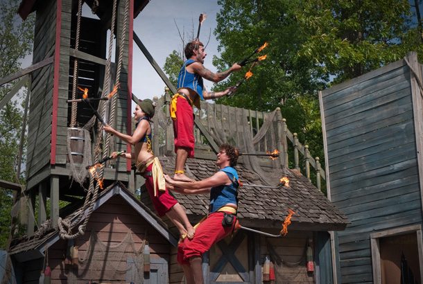 three acrobats standing atop each other with fire