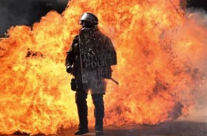 A greek policeman stands next to a wall of flames during the anti-austerity protest