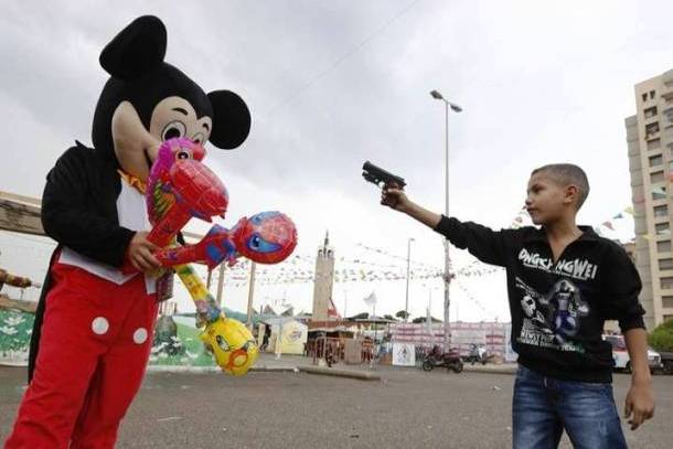 A boy points a toy gun to a Mickey Mouse mascot