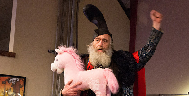 A bearded man with a boot on his head holding a pink stuffed pony