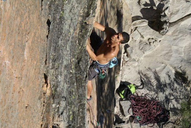man rock climbs shirtless on sheet cliffface