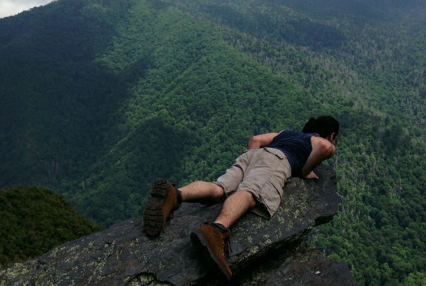 man laying flat on rock looking over valley