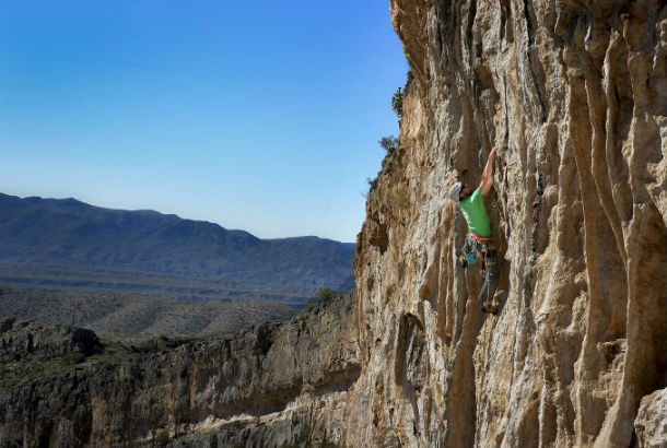 climber climbing rockface with mountains in background