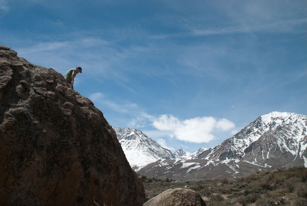 man sitting on top of mountain with snowcapped peak in background