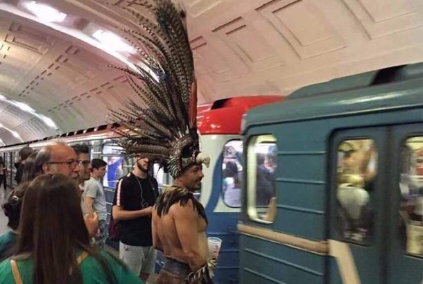 man with large feathered headdress stands outside subway car