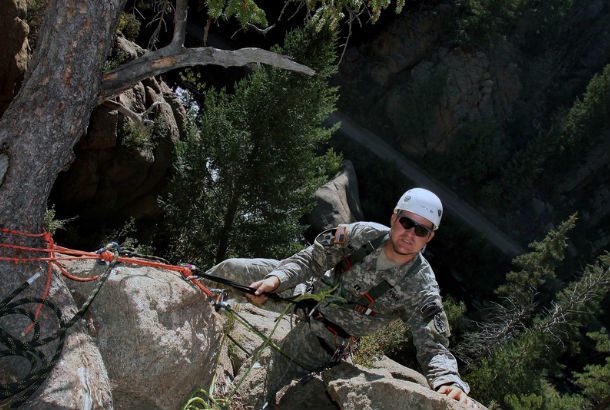 Man in camouflage ties onto tree and begins decent down the mountain