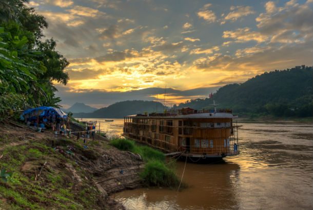 The Mekong River from one bank at sunset with small ferry docked at shore
