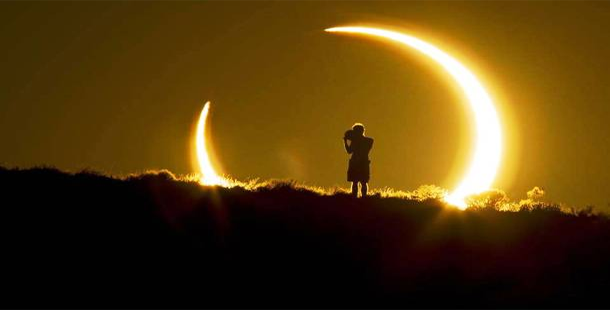 A silhouette of a person standing on a hill with a couple of solar eclipses