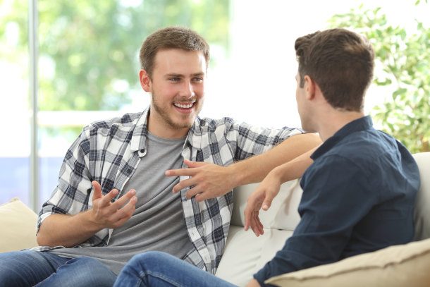 two guys smiling and talking on couch