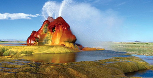 A geyser erupting in a body of water with fly geyser in the background