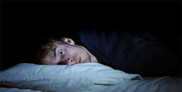 A person lying in bed with his head on a pillow, surprising effects sleep deprivation