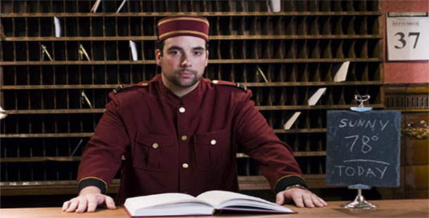 A staff hotel person in uniform sitting at a desk with a book