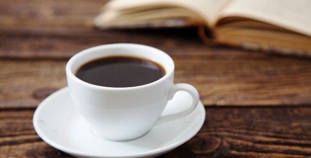 A cup of coffee on a saucer next to a book