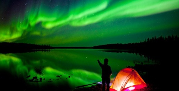 A person standing next to a tent and a green aurora borealis