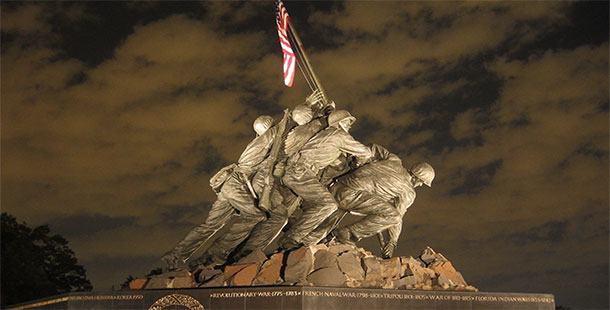 A statue of soldiers holding a flag with marine corps war memorial in the background