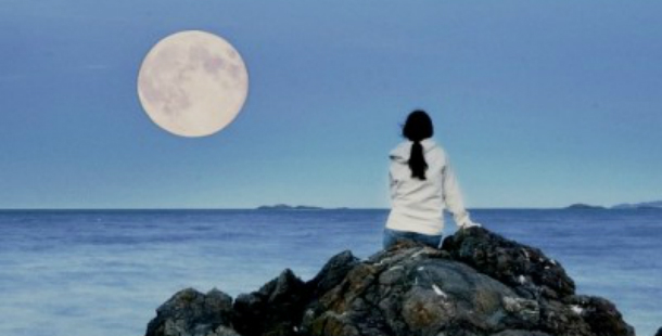 A person sitting on a rock looking at the full moon