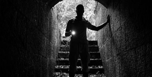 A person standing in a tunnel with a flashlight, unsolved mysteries