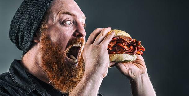 A person with a beard eating a sandwich