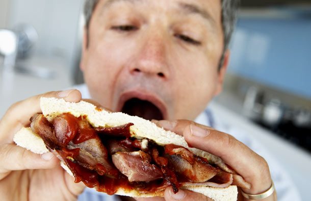 Middle aged man eating a bacon sandwich