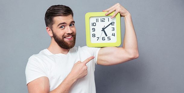 A bearded man holding and pointing at a wall clock