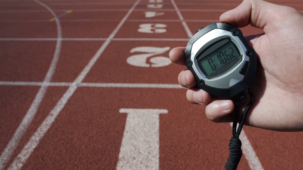 A hand holding a stopwatch on a running track