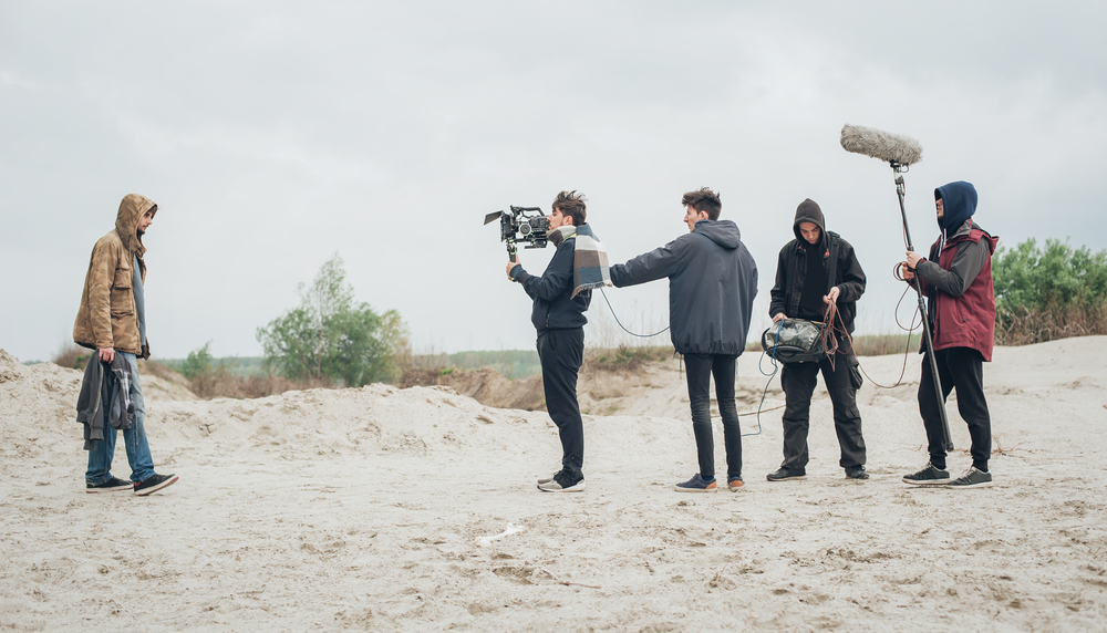 A group of people filming in a sandy area
