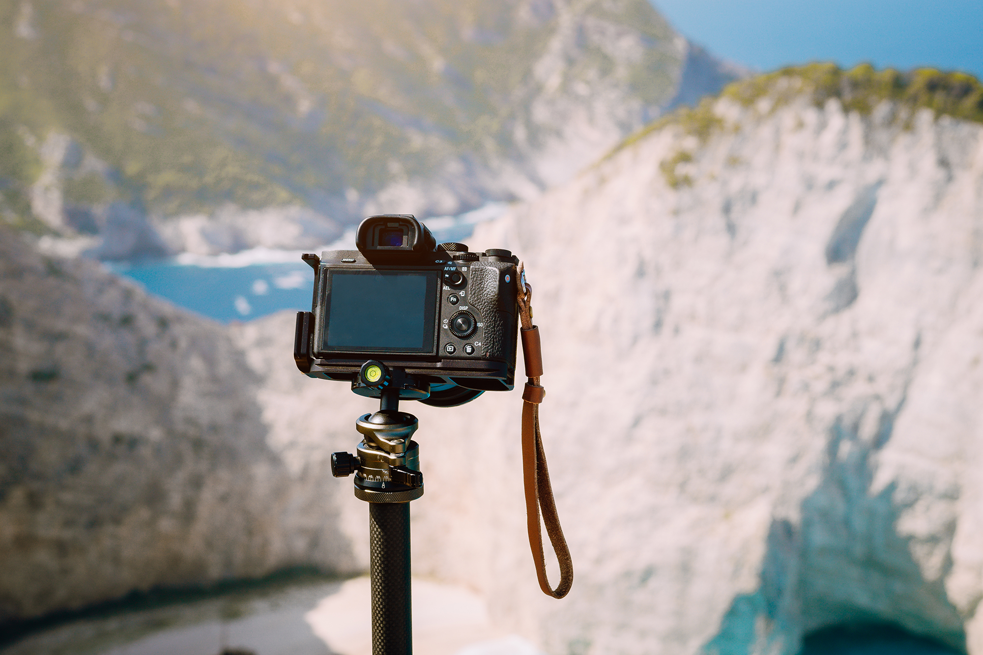 Digital photo camera on tripod against huge cliff rocks of Navagio beach in morning sun light. Famous visiting landmark location on Zakynthos island, Greece.
