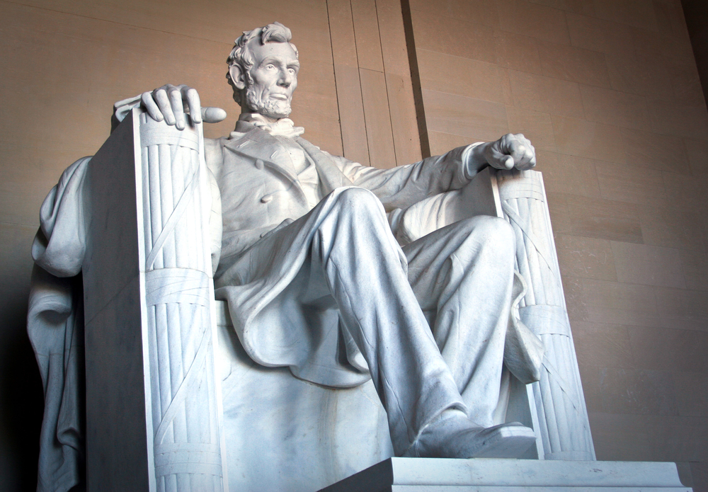 A statue of a person sitting in a chair with lincoln memorial in the background